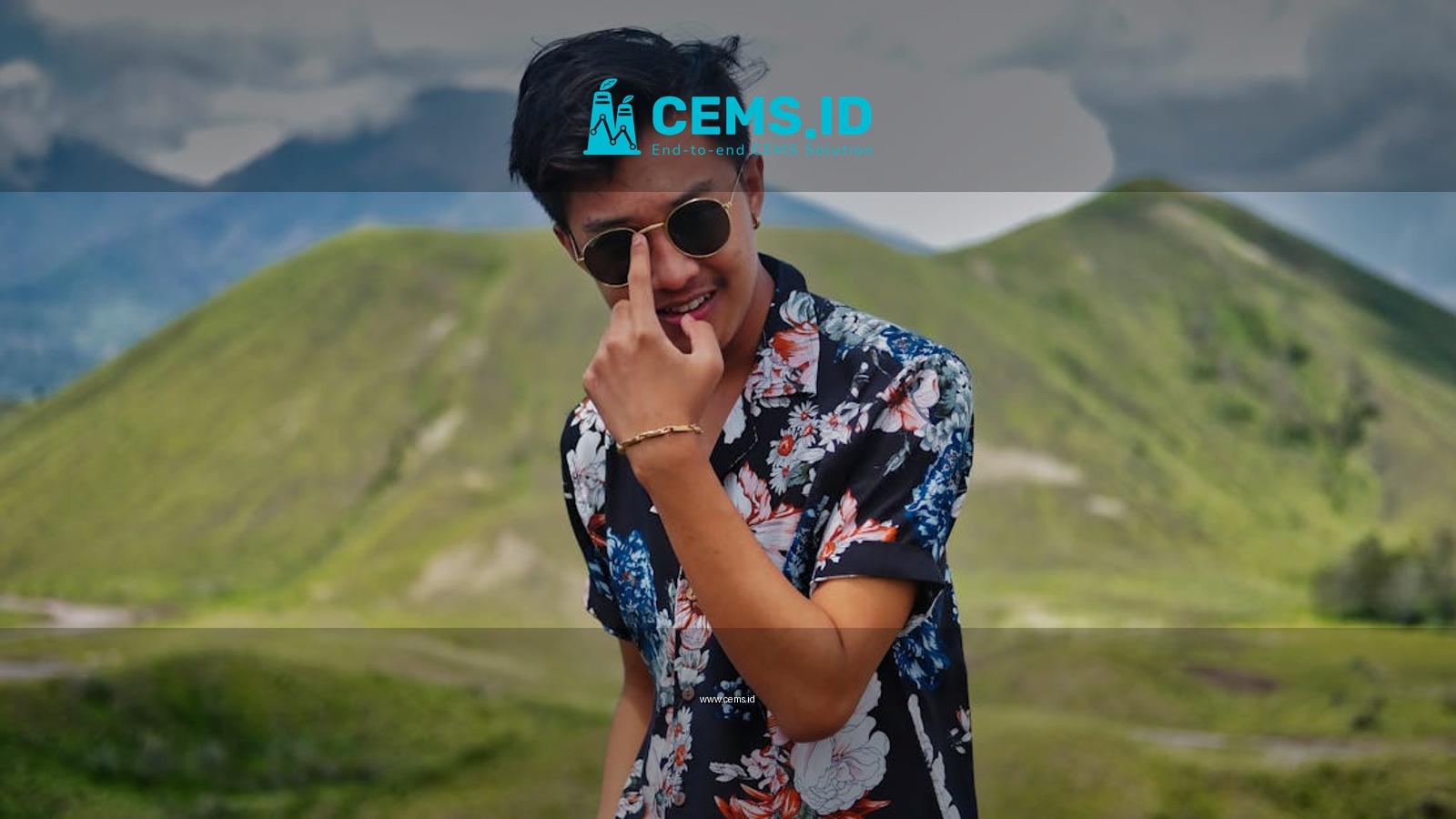 A fashionable man wearing sunglasses in a scenic Indonesian mountain landscape, exuding style and adventure.