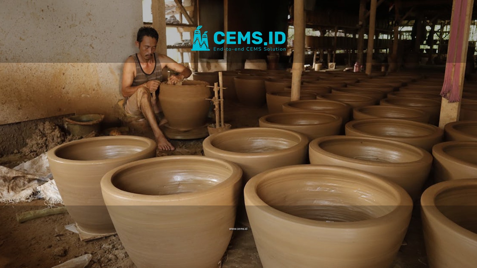 An artisan focuses on crafting large clay pots in a traditional indoor pottery workshop.