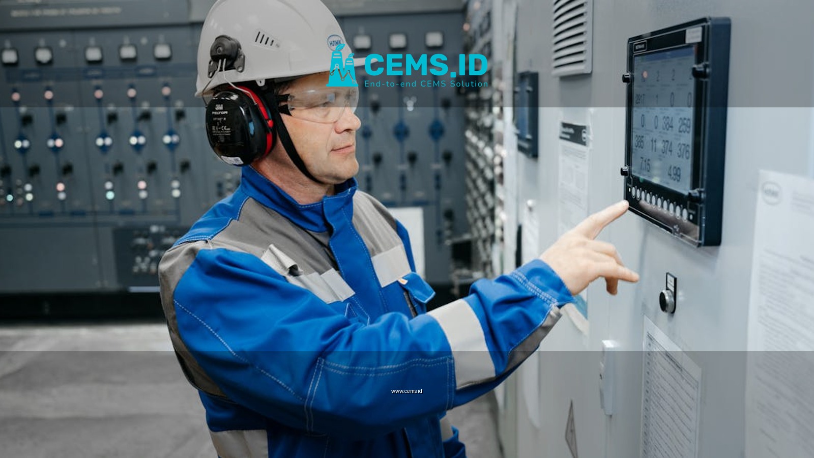 Technician in safety gear working at an industrial control panel indoors.