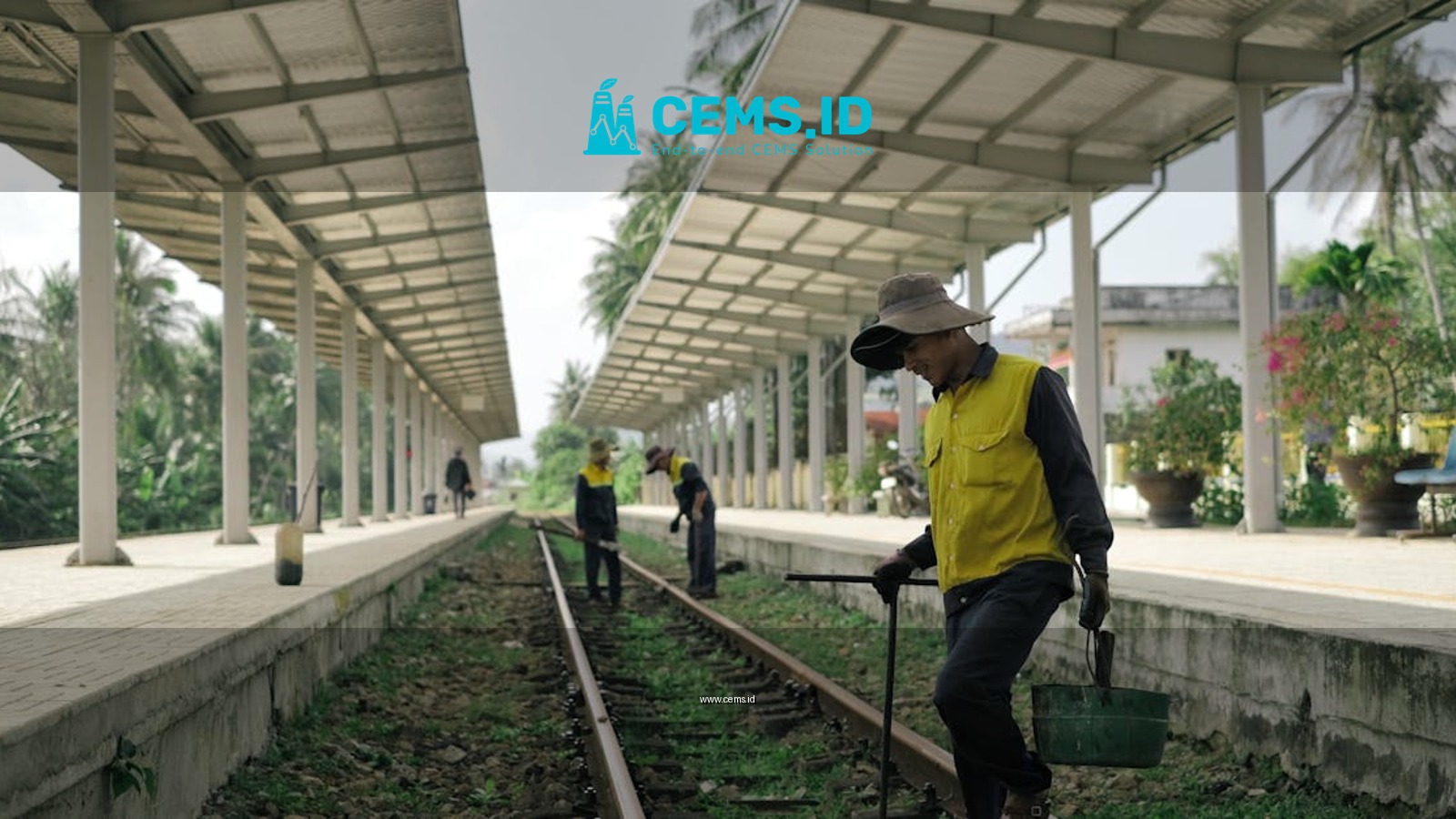 Workers maintaining railway tracks at a tropical outdoor train station.