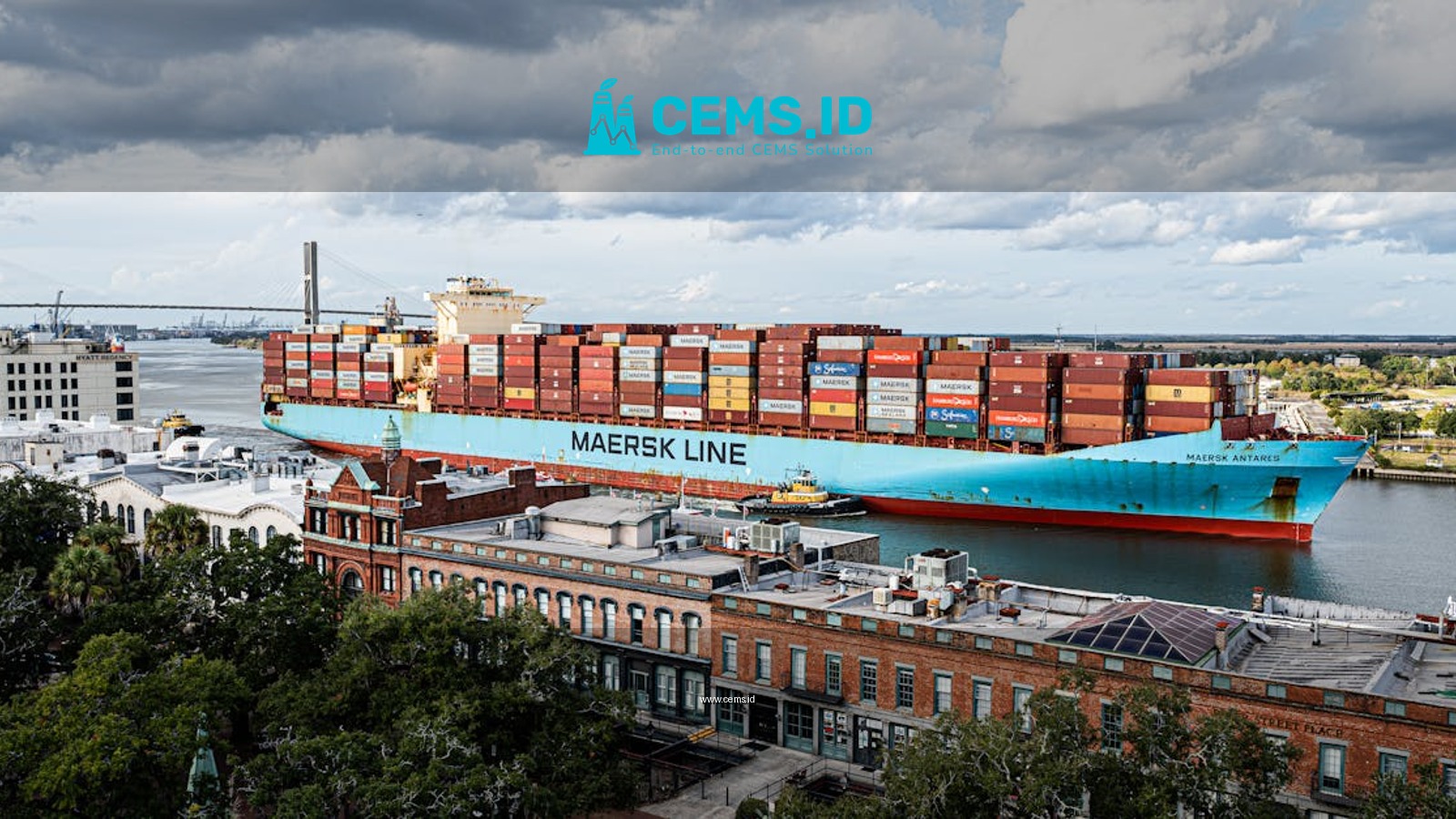 Aerial view of a cargo ship on the Savannah River with a city backdrop and cloudy sky.