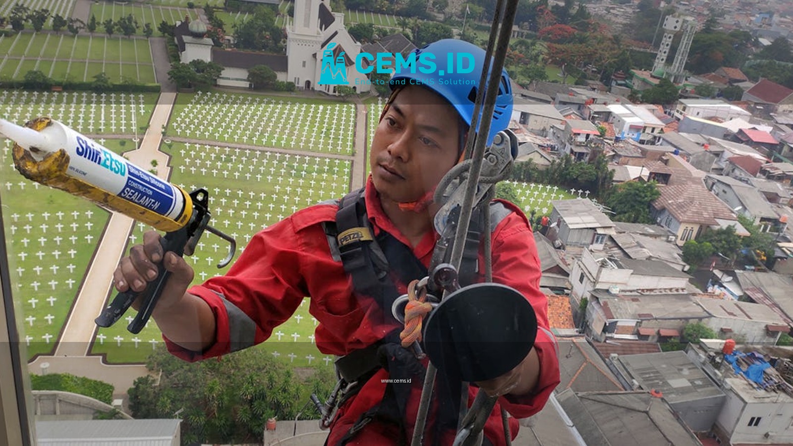 A professional window cleaner in Jakarta using safety gear and sealant with a cityscape vista backdrop.