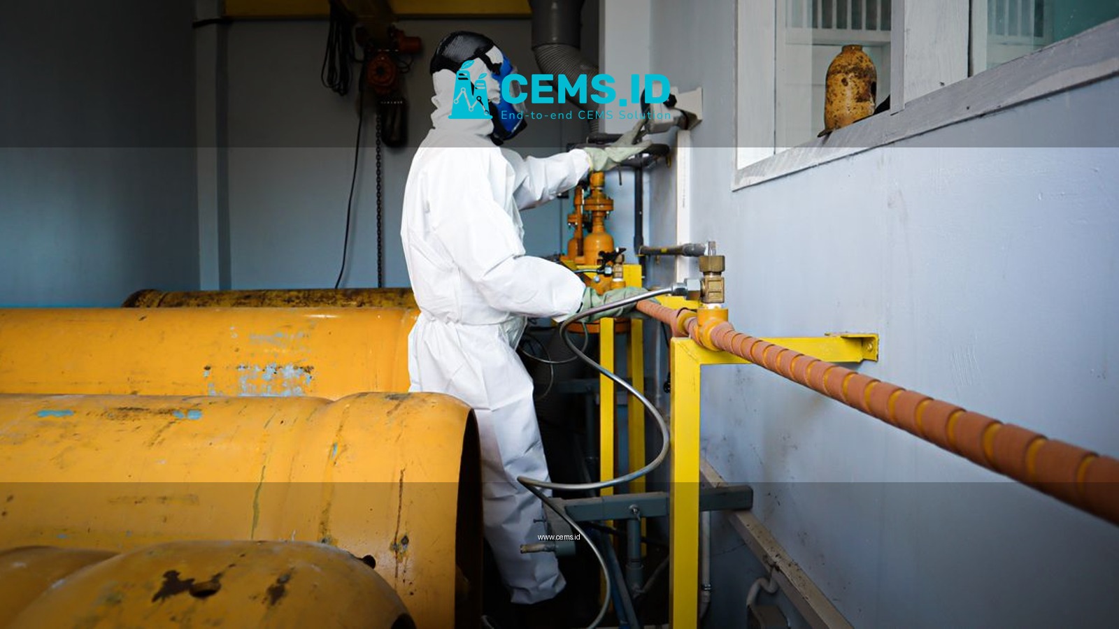 Worker in full protective suit and gas mask handles industrial pipes indoors in Indonesia.
