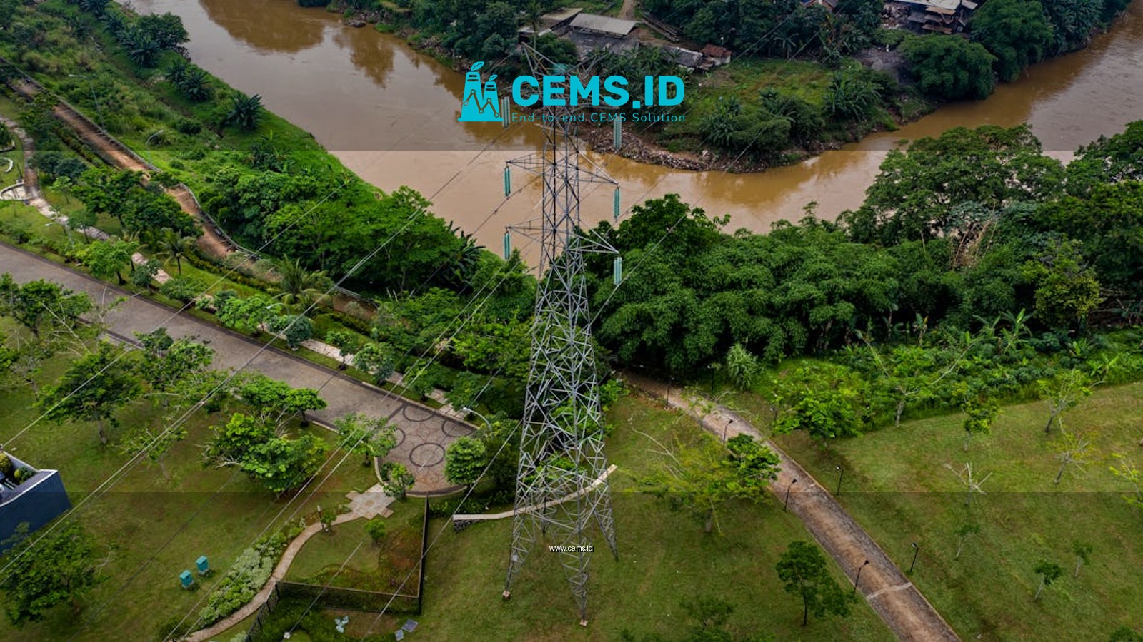 Aerial view of powerlines crossing over lush greenery and a river in Sindang Jaya, Banten, Indonesia.