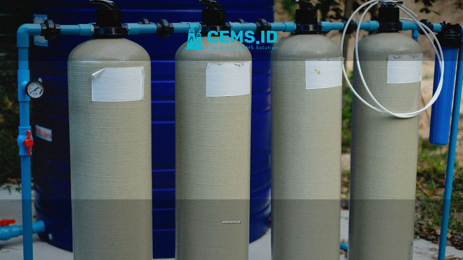 Four beige tanks in an outdoor water treatment setup with blue piping.