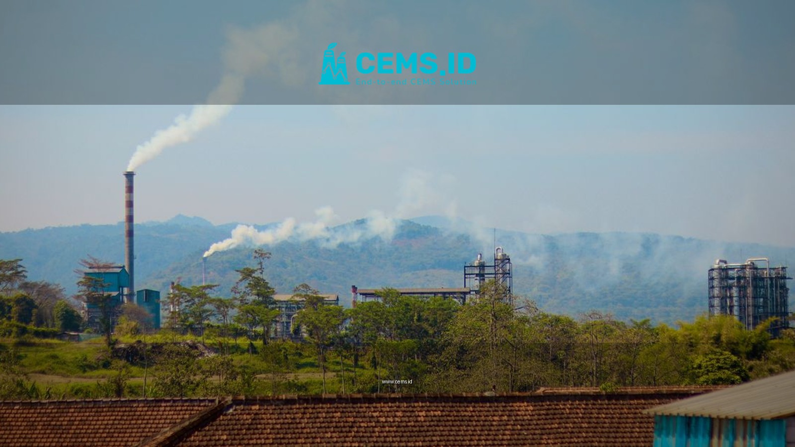 Industrial plant emitting smoke in a lush green area with mountains in the background, indicating pollution