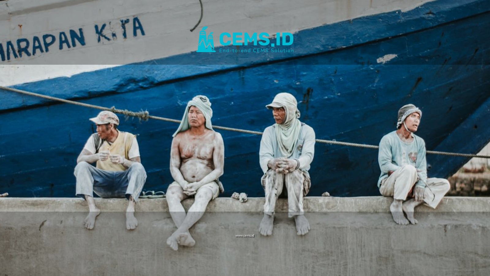 Four dock workers rest on a pier beside a large blue ship, reflecting a moment of pause.