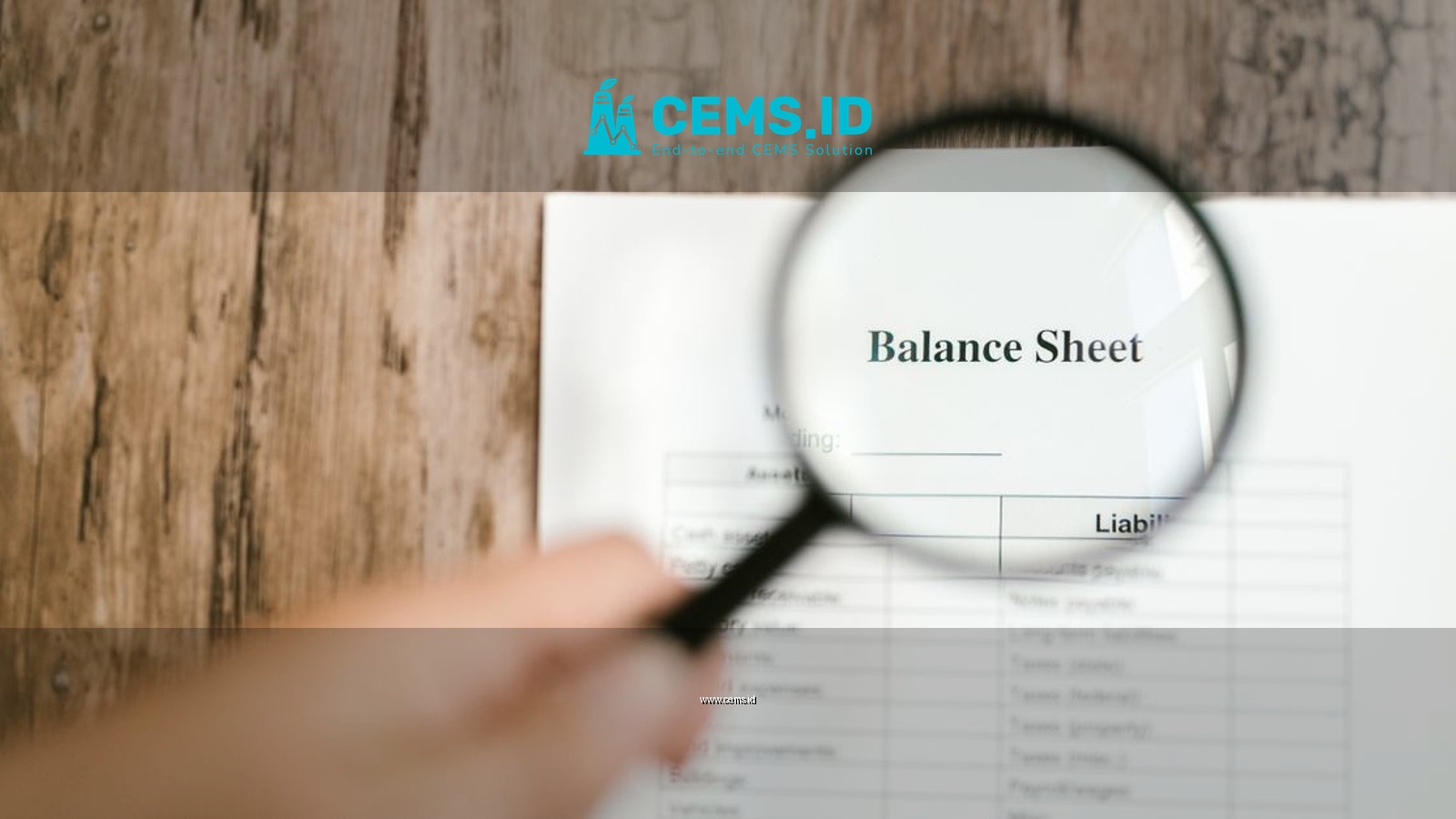 Close-up of a balance sheet document on wooden surface with a magnifying glass held by a hand.