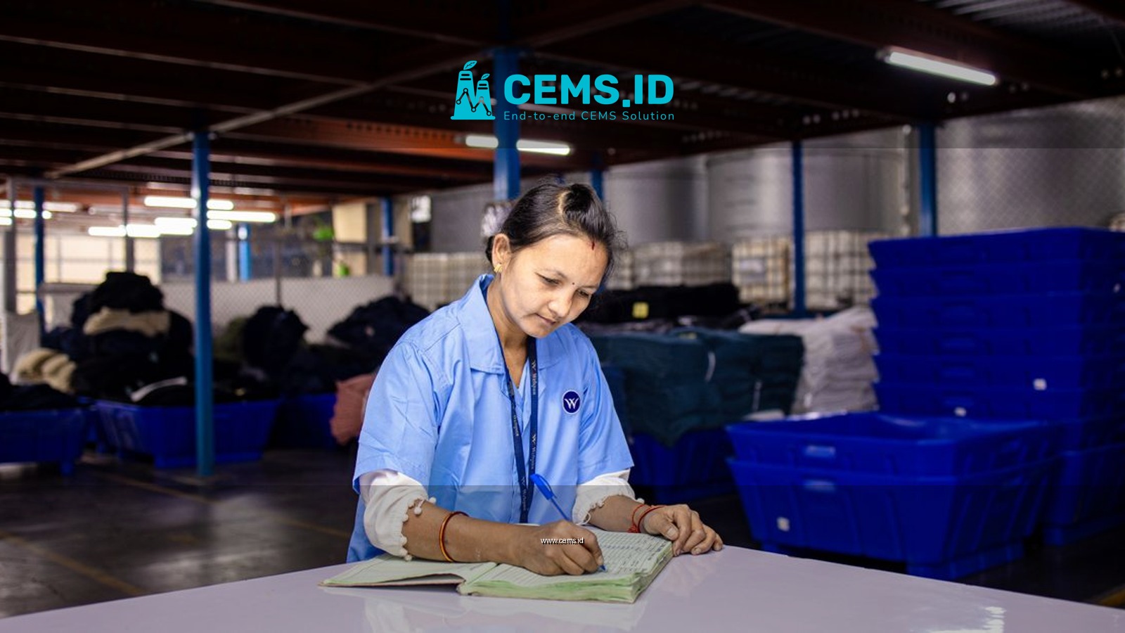 Woman in blue uniform taking notes in an industrial warehouse setting.