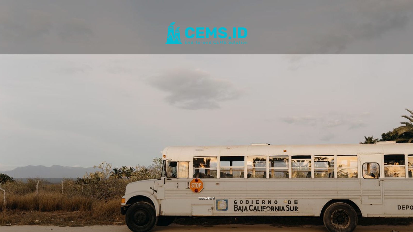 A white school bus parked in the desert landscape of Baja California Sur, Mexico under a clear sky.