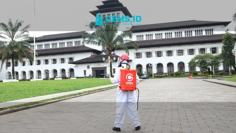 A person in protective clothing disinfects an area in front of a historic building with palm trees.