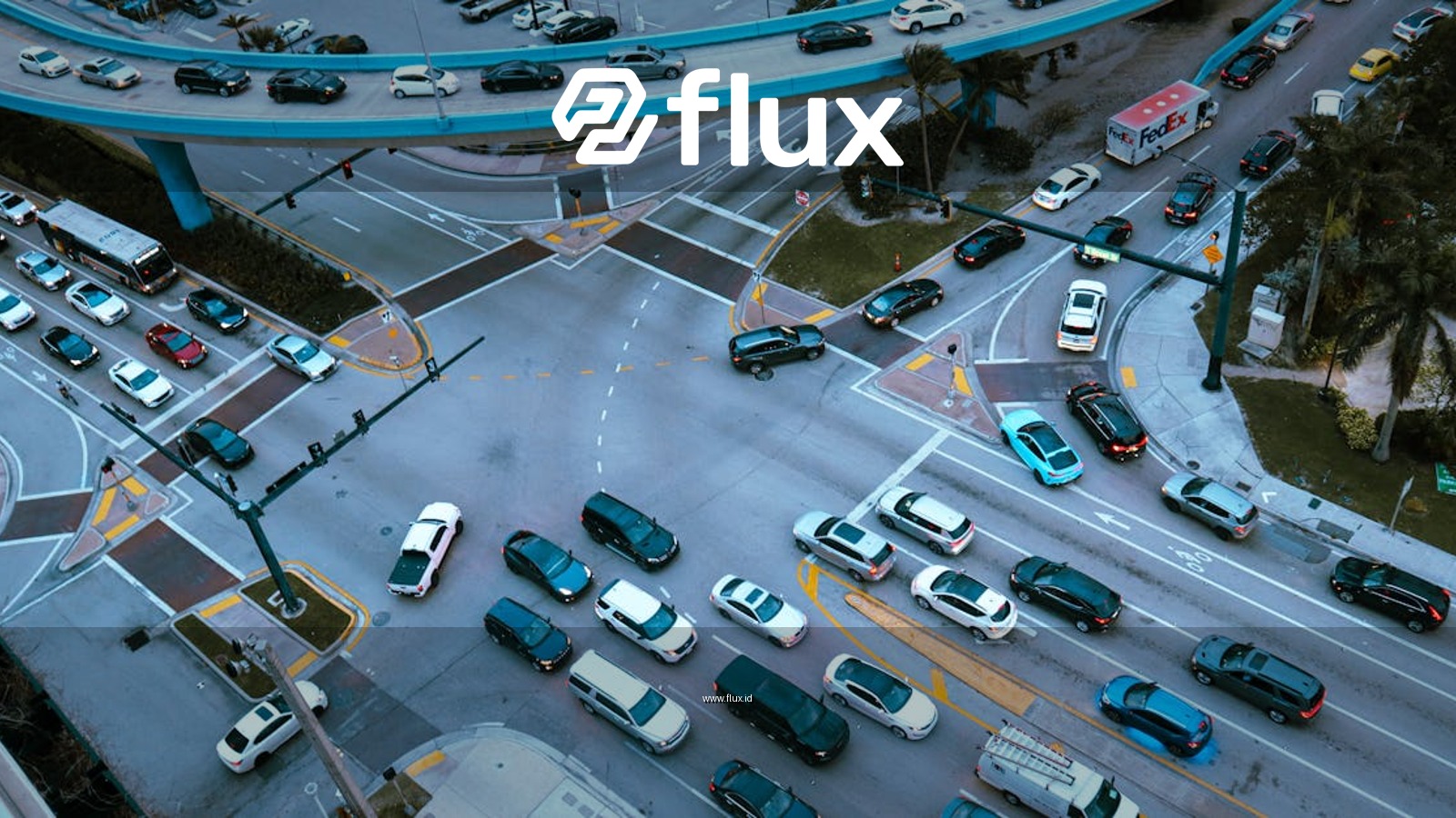 Aerial view of a busy urban intersection filled with cars and traffic under a blue overpass.