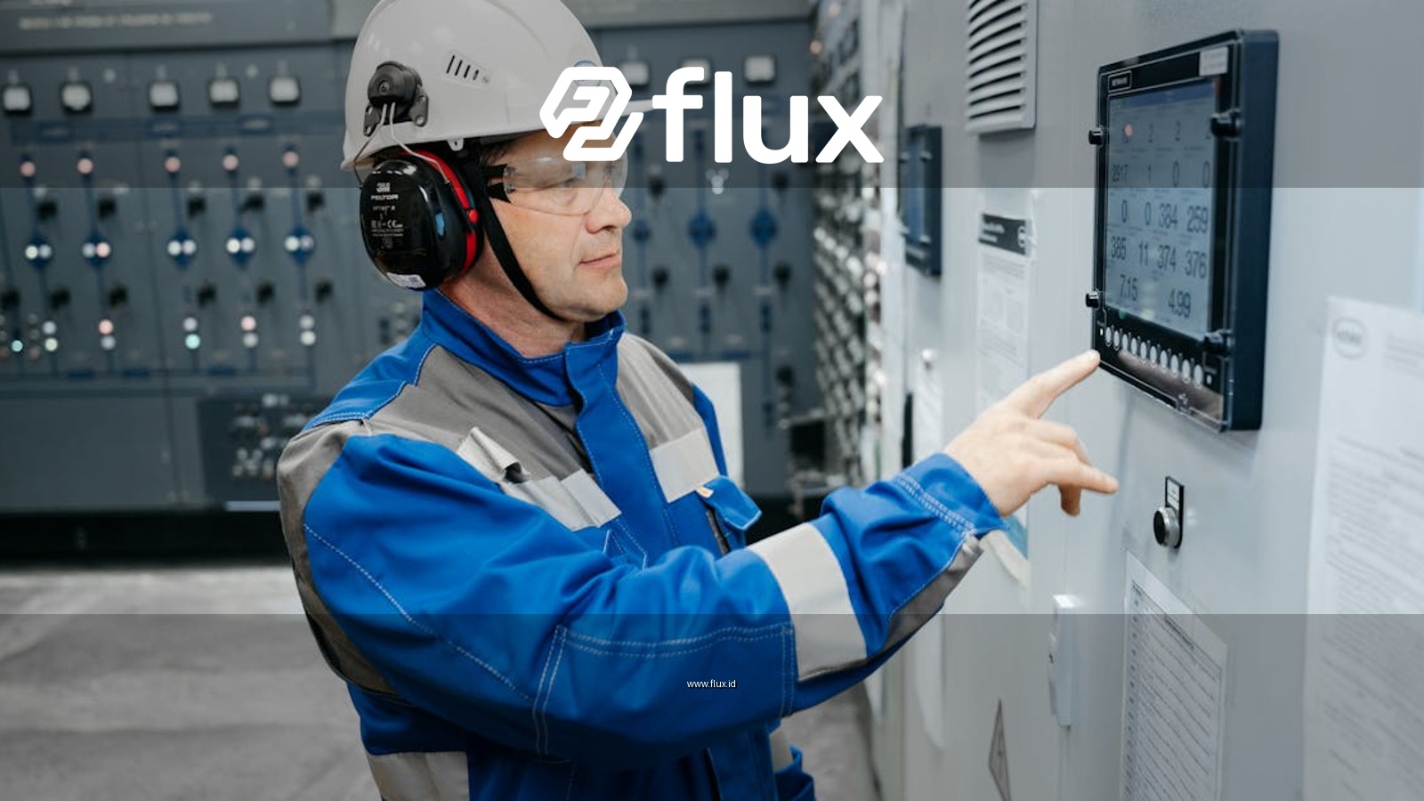 Technician in safety gear working at an industrial control panel indoors.