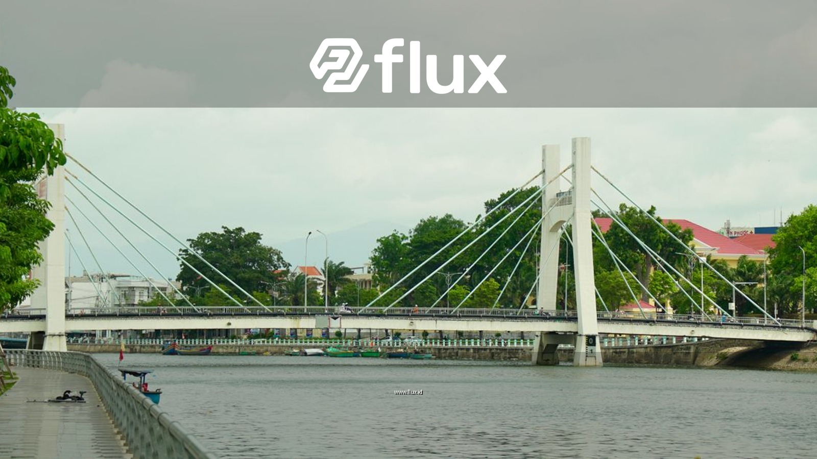 A scenic view of a modern suspension bridge crossing a tranquil river lined with trees.