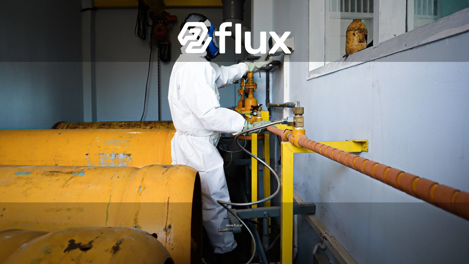 Worker in full protective suit and gas mask handles industrial pipes indoors in Indonesia.