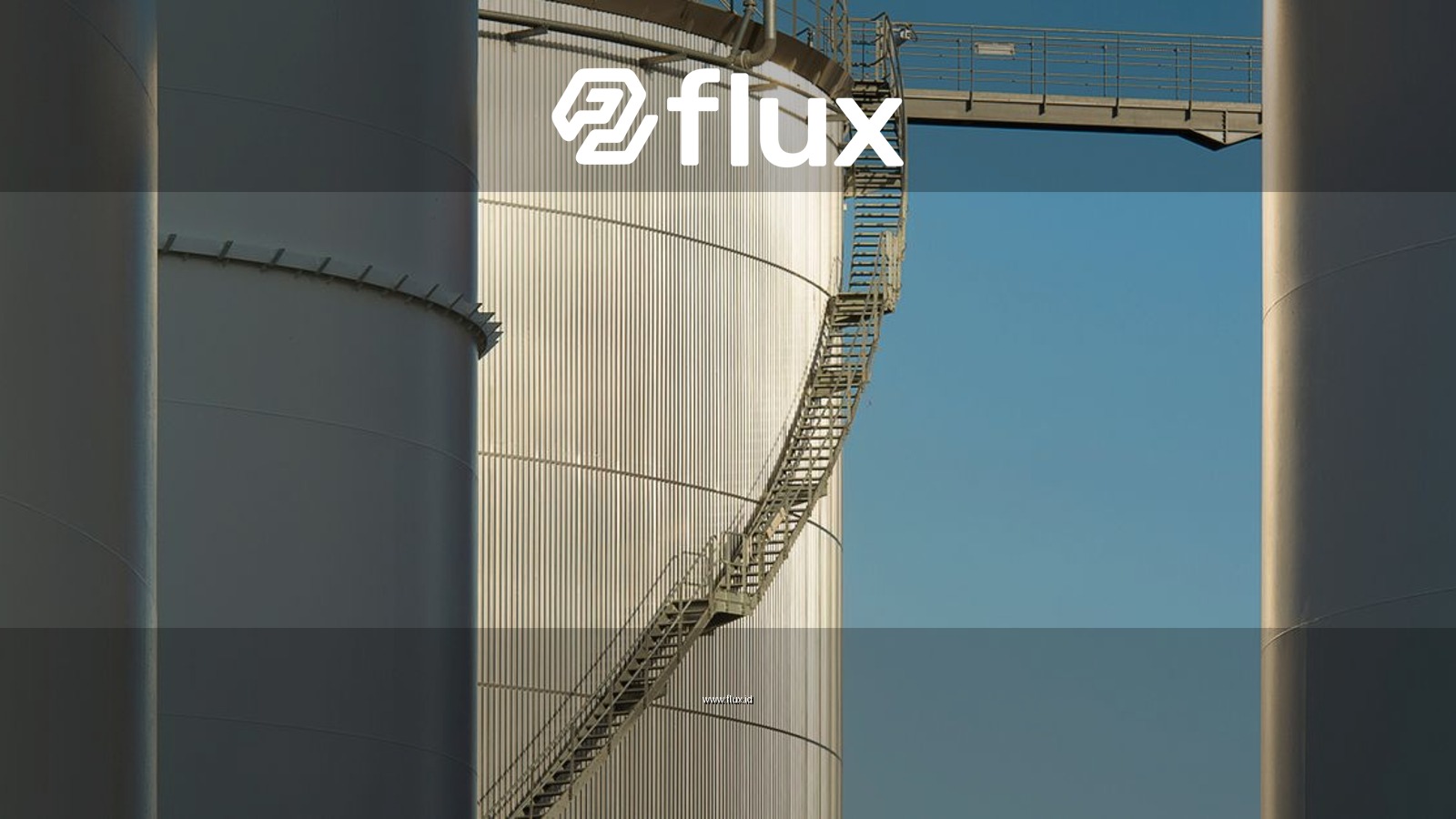 Close-up view of metal industrial silos with a connecting staircase against a clear blue sky.