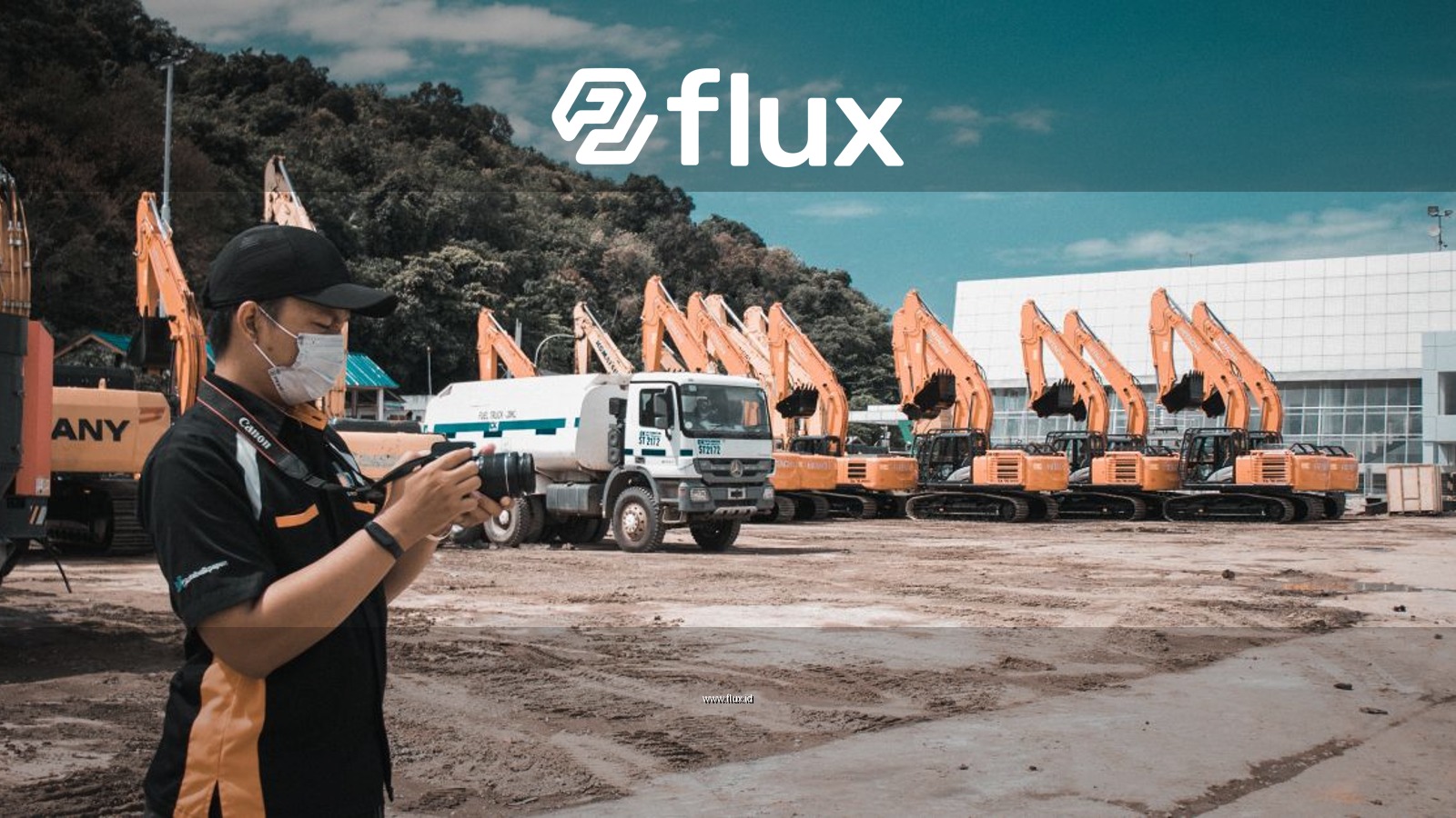A photographer takes photos at a construction site with heavy machinery and trucks on a sunny day.
