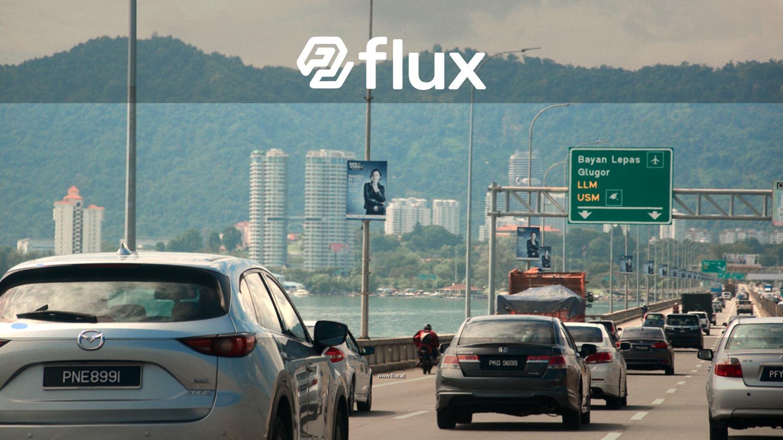 Busy day on Penang Bridge with cars traveling under a cloudy sky, featuring mountains and cityscape.