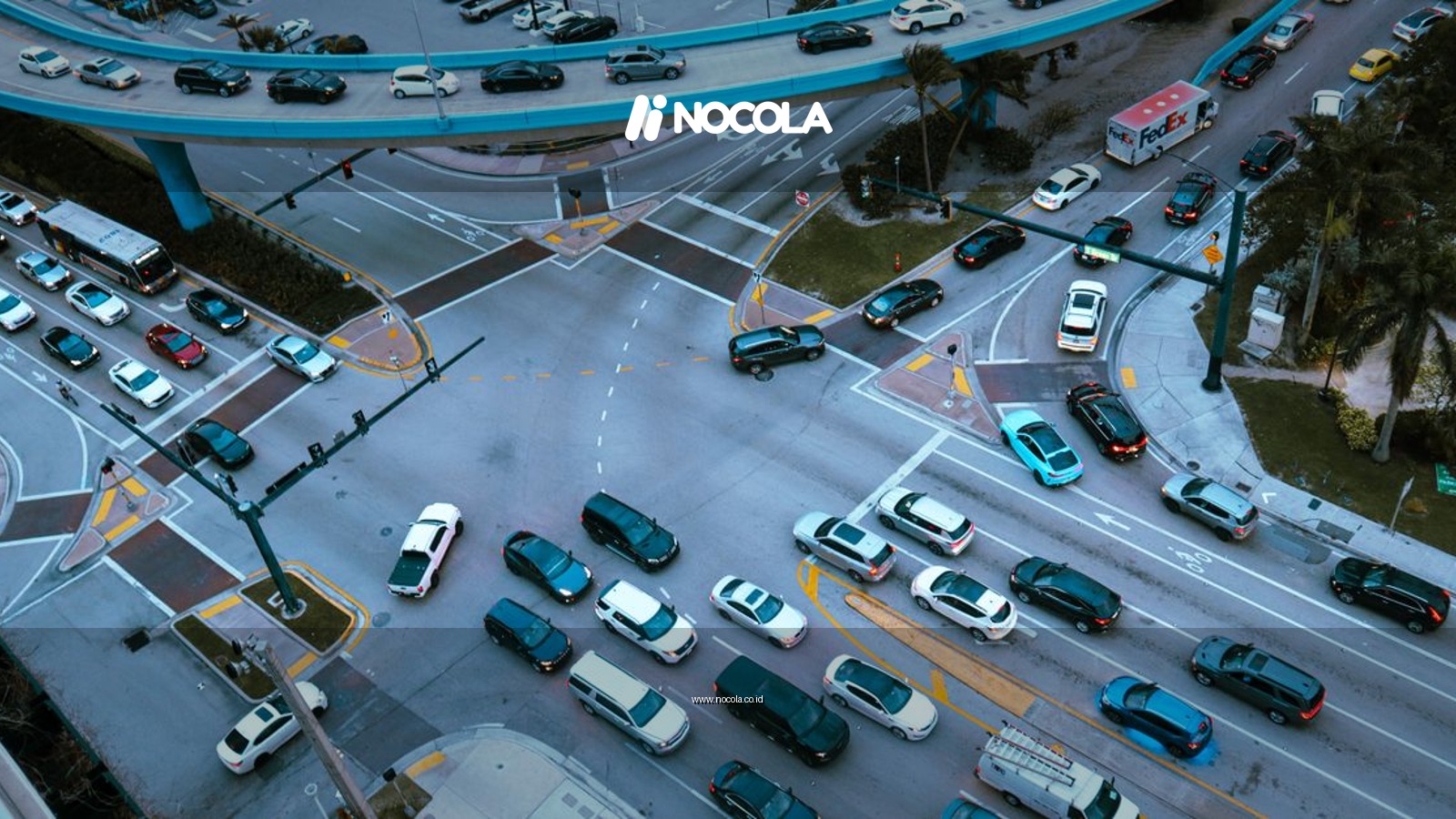 Aerial view of a busy urban intersection filled with cars and traffic under a blue overpass.