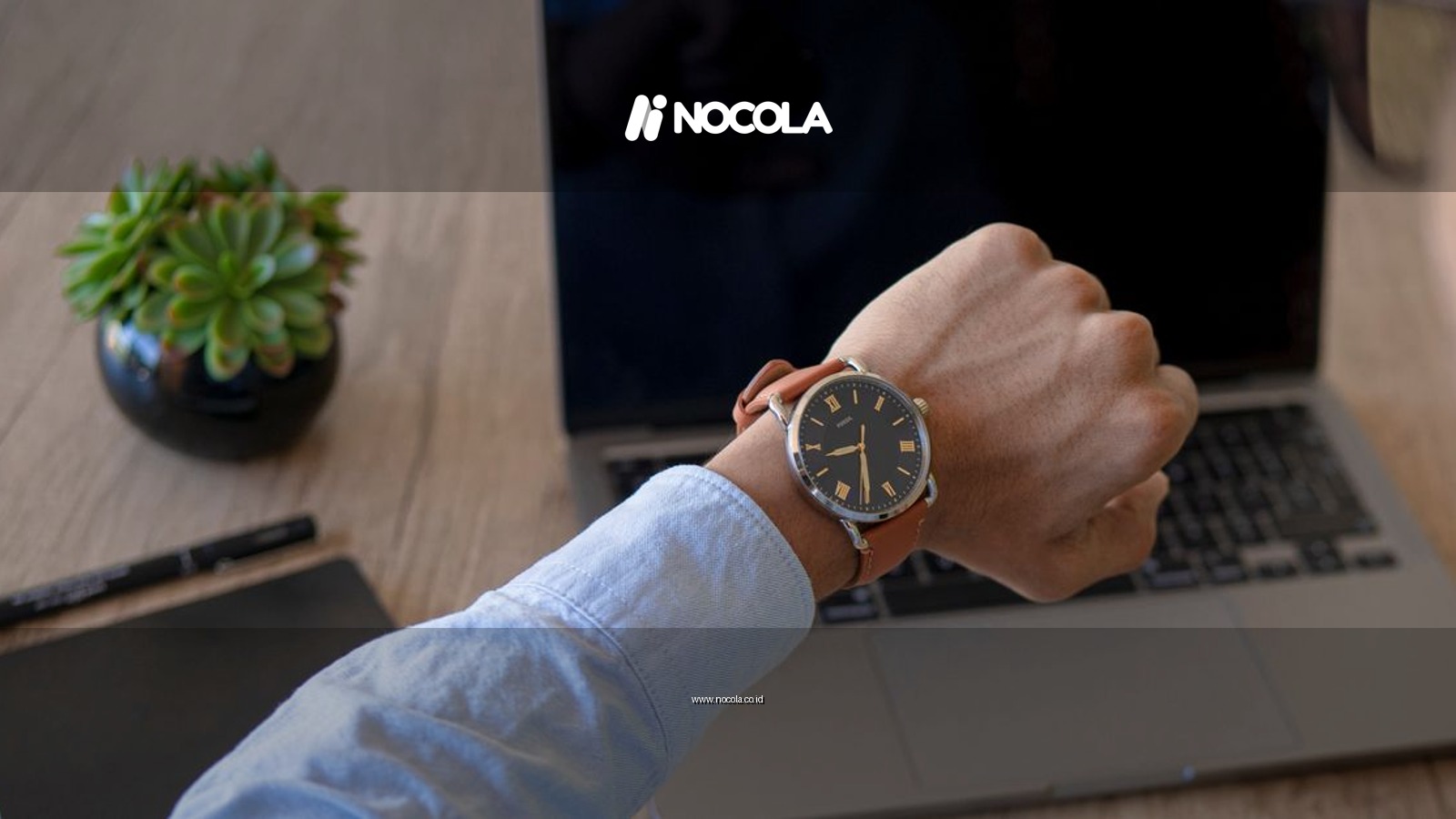 Adult male checks time on watch while working on a laptop at home office.