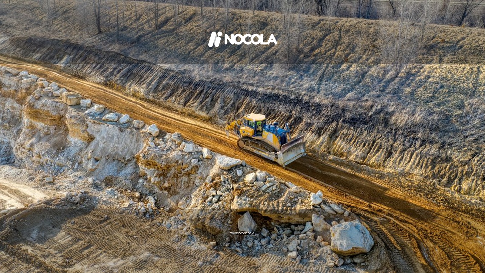 An aerial view of a bulldozer operating on a rocky terrain in a quarry setting during daylight.