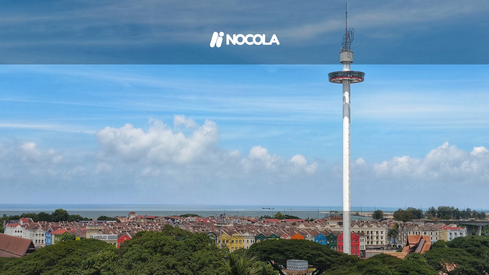 Aerial view of Malacca City skyline featuring Menara Taming Sari against a blue sky.