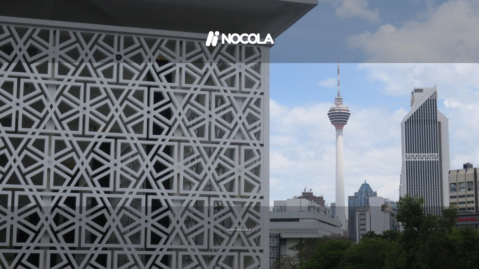 A view of Kuala Lumpur Tower amidst modern buildings and intricate architecture, under a clear sky.