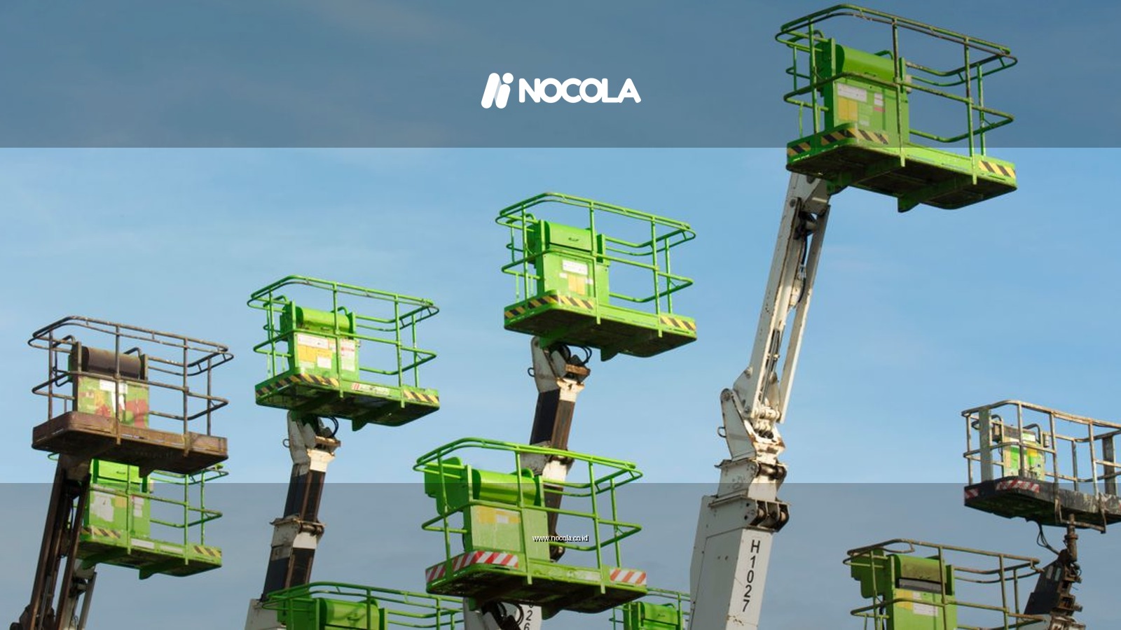A group of green cherry pickers extending against a clear blue sky in an industrial setting.