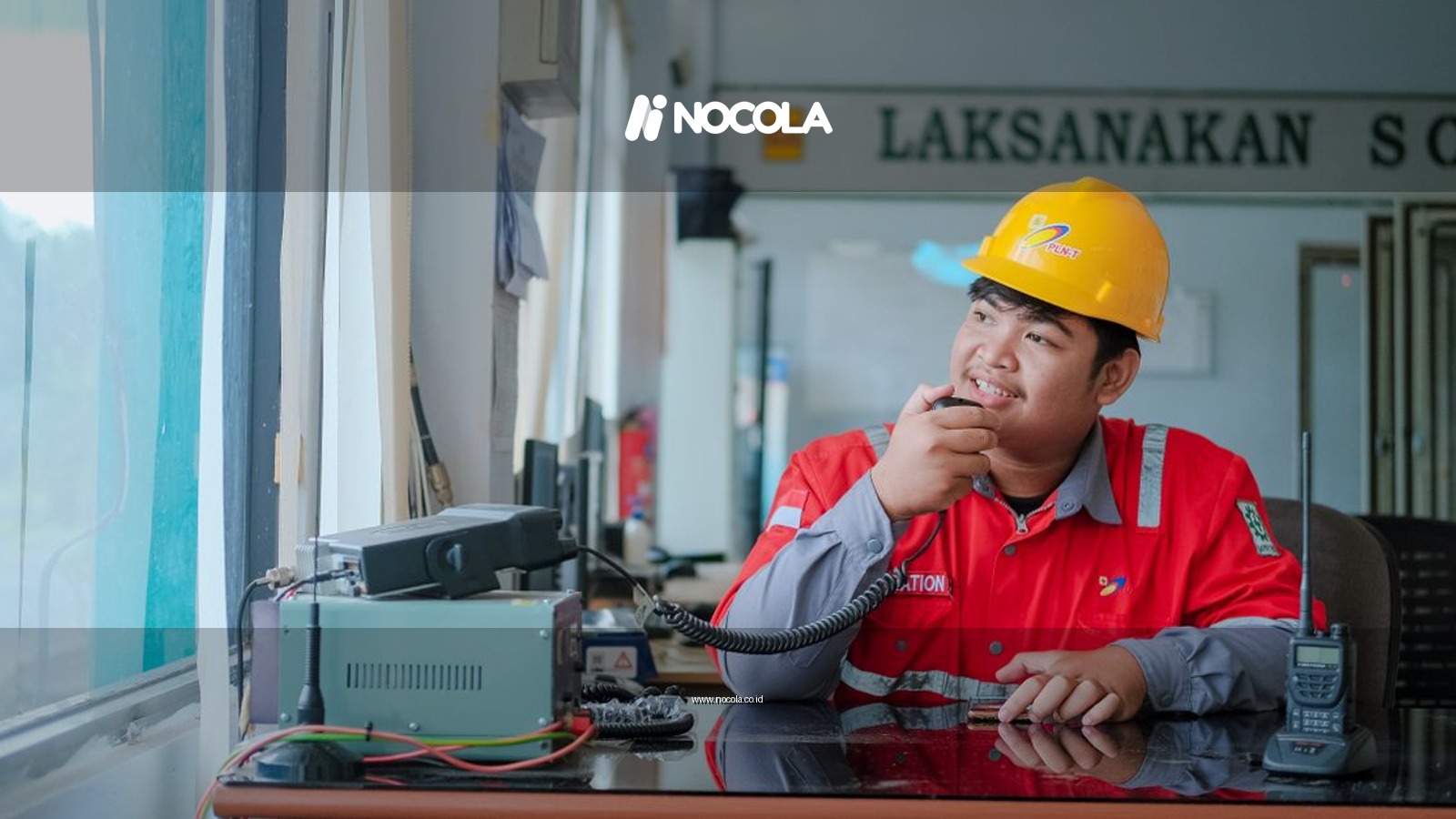 Smiling construction worker in hard hat using a two-way radio indoors for communication.