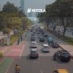 A bustling urban roadway in Jakarta with cars, motorbikes, and a bus stop in view.