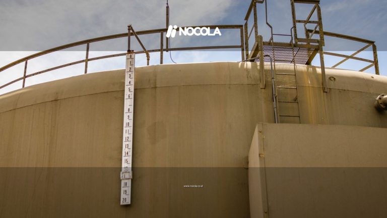 A low angle view of a large industrial water tank with a measuring scale and ladder under a clear sky.
