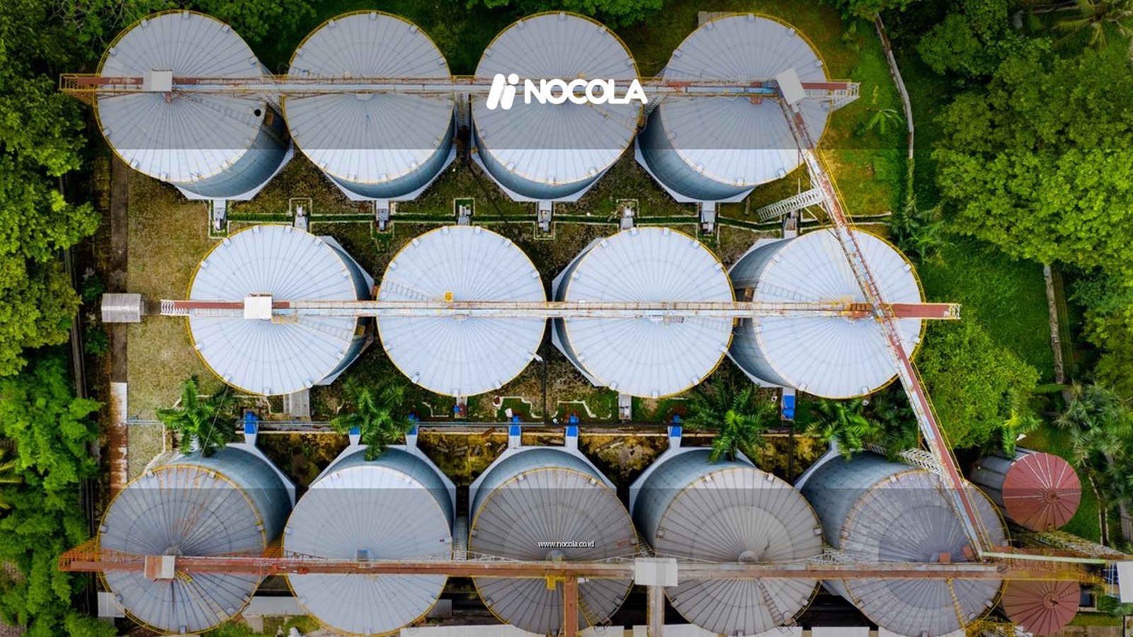 Aerial shot of metal storage tanks surrounded by green foliage in an industrial plant.