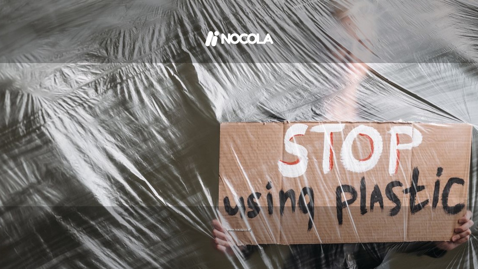 A person holds a cardboard sign reading 'STOP using plastic' behind a plastic sheet, conveying an environmental message.