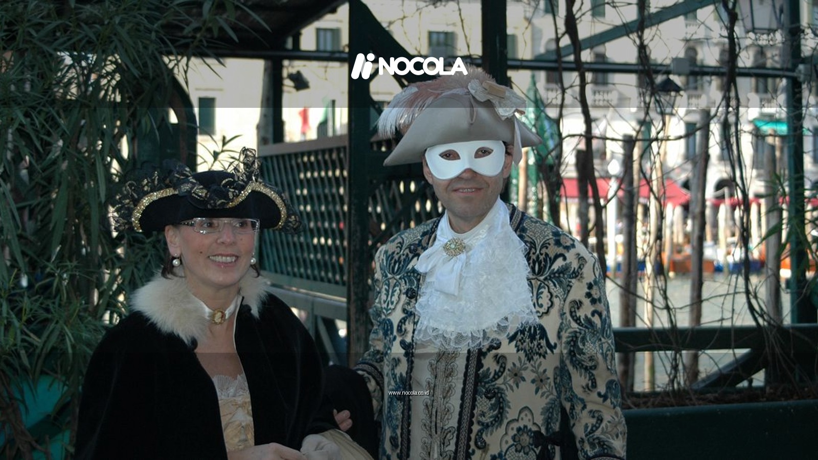 Two adults in ornate Venetian costumes at an outdoor carnival event.