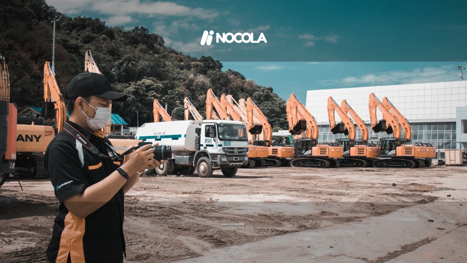 A photographer takes photos at a construction site with heavy machinery and trucks on a sunny day.
