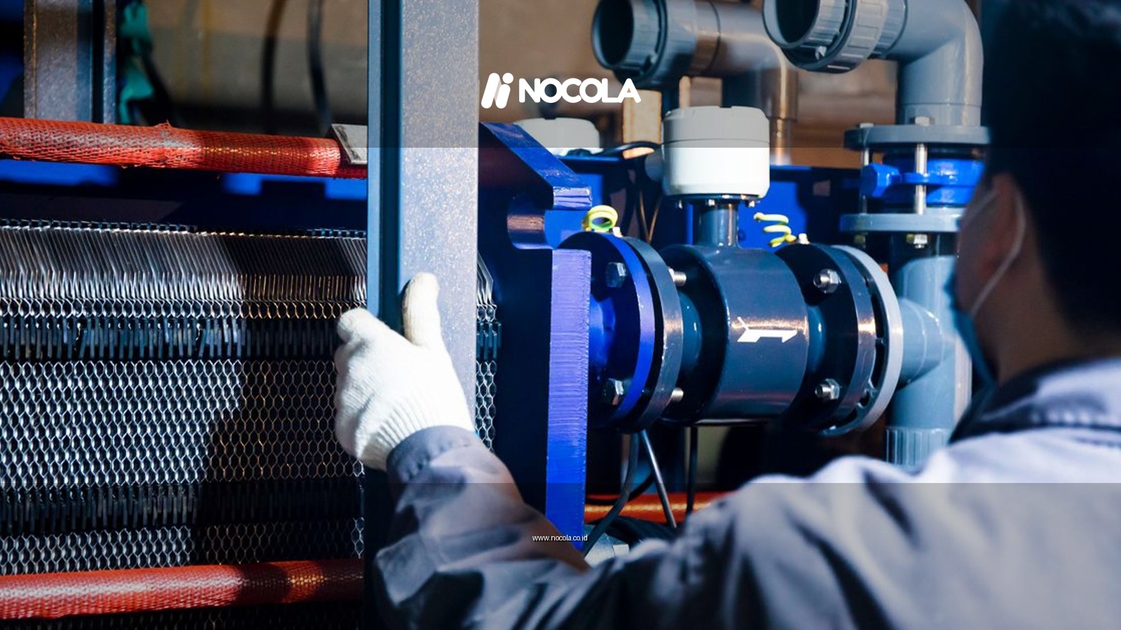 A worker in blue sleeves inspects machinery pipes and equipment at an industrial plant.