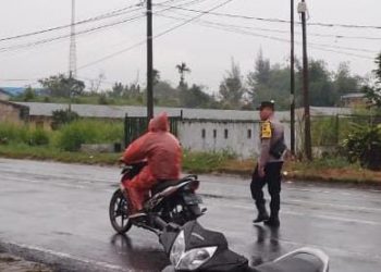 Meski hujan turun, Bhabinkamtibmas Polsek Raya, Aipda Joni Susanto Purba, tetap menjalankan tugasnya mengatur lalu lintas di Simpang Sekolah SD Bintang Timur, Kelurahan Sondi Raya, Kecamatan Raya, Kabupaten Simalungun, pada Jumat (14/03/2025)( Ist/Susan/ Nawasenanews)