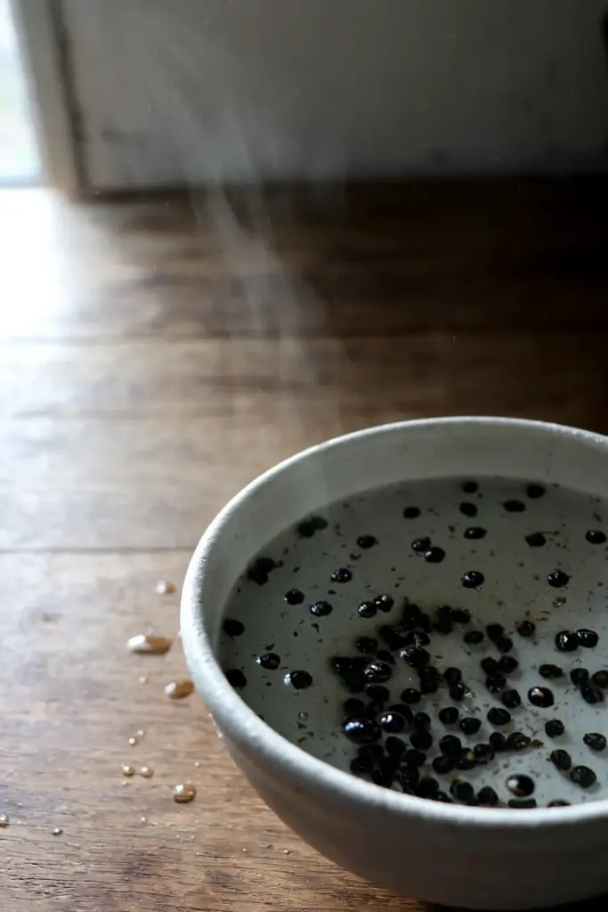 Andaliman seeds soaking in a bowl of hot water with faint steam rising