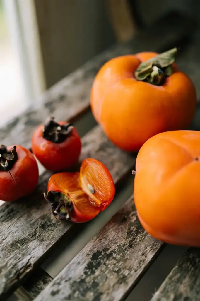 Small American persimmons beside large Fuyu persimmons on a bench