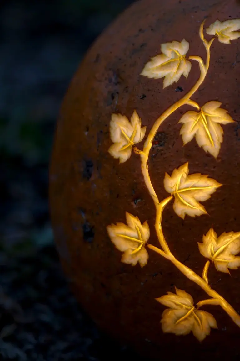 Close view of a pumpkin etched with a curling leaf and vine pattern glowing gold through the thinned flesh