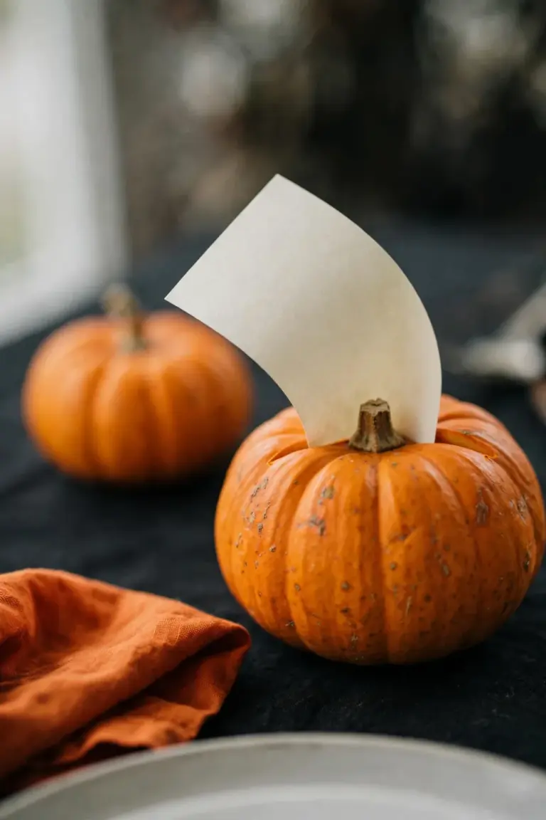 Mini orange pumpkin holding a cream place card in a slit at a set table