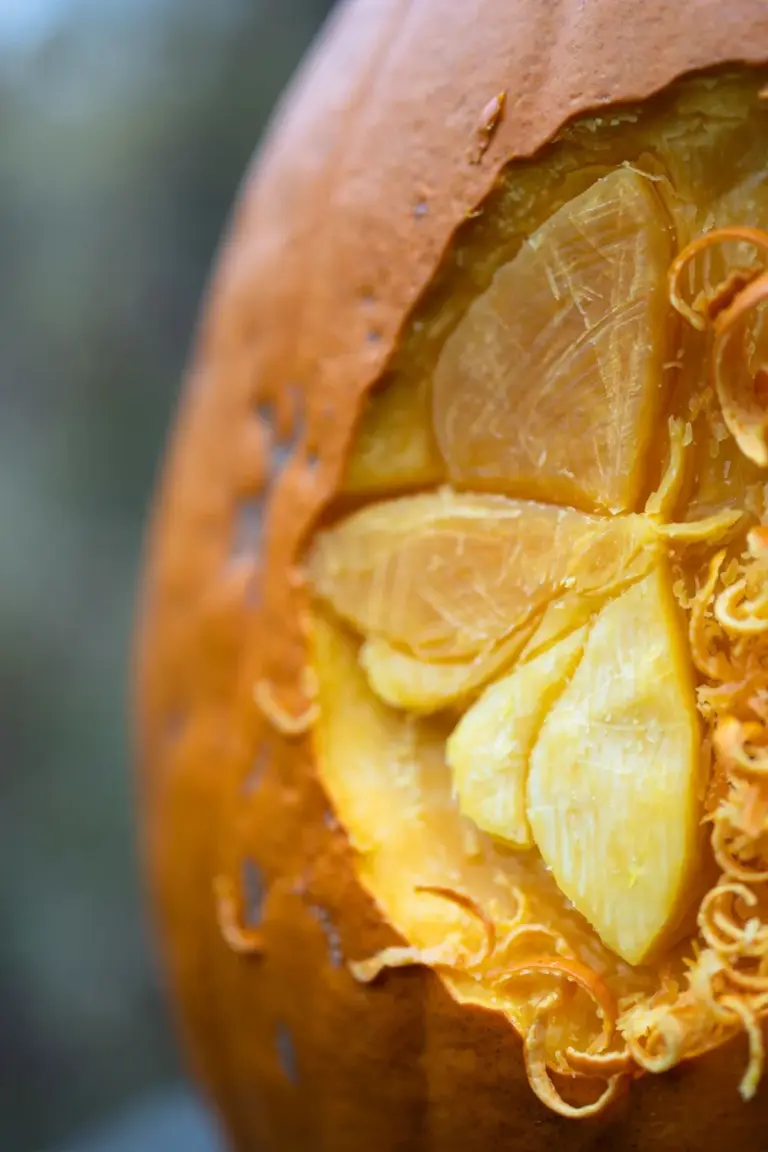 Close view of a pumpkin rind etched with a moth in two depths, shallow cuts glowing dim gold beside deep bright cuts