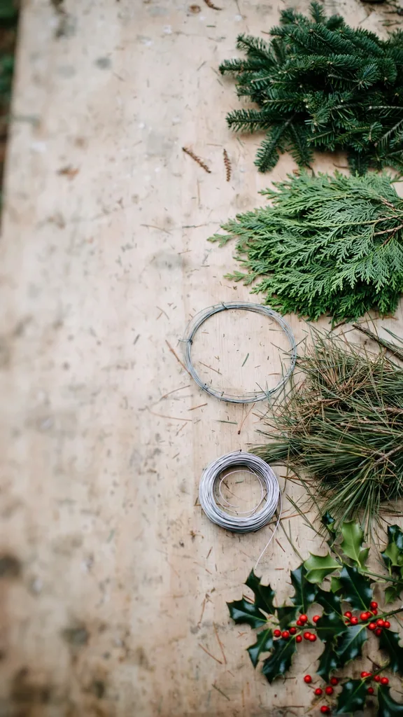 Wreath materials on a workbench: fir, cedar, pine, holly, wire, and a round frame