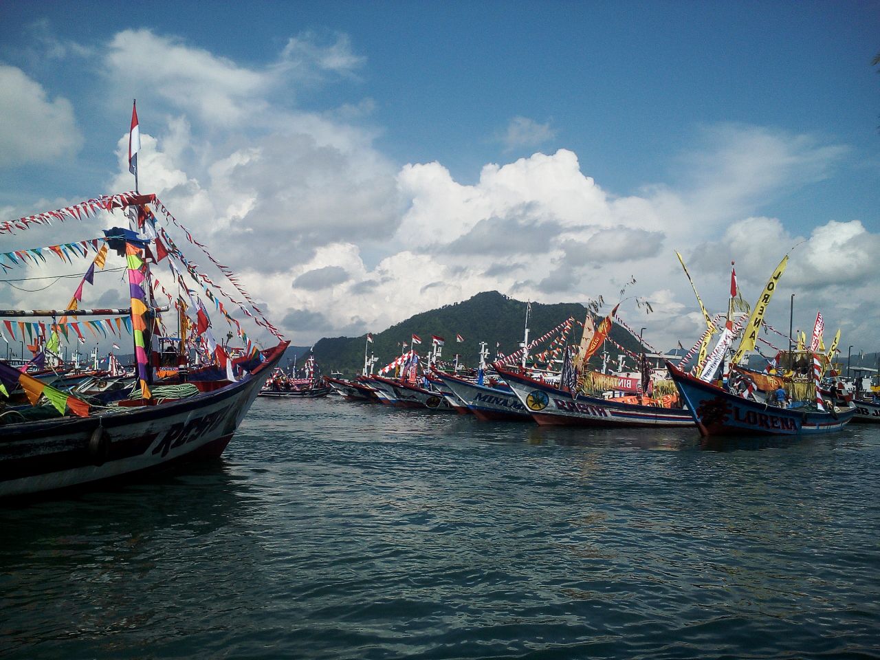 Deretan kapal nelayan mengiringi tumpeng agung dan sesaji