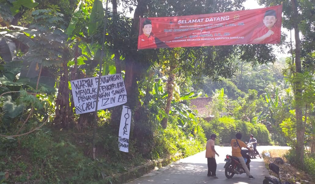 Poster Tolak Tambang di bawah poster sambutan kunjungan DPR RI dan Bupati