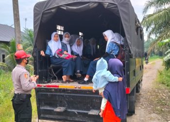 Personel SPN Polda Sumut, Aipda Zulkifli Sirait dengan sigap membantu mengantar anak-anak di Desa Cempa yang akan berangkat sekolah (foto : Polda Sumut)