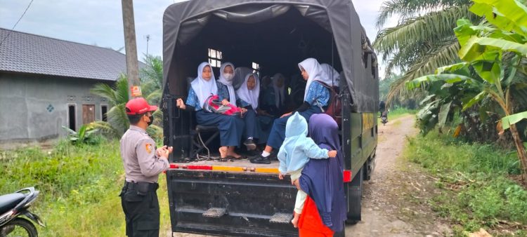 Personel SPN Polda Sumut, Aipda Zulkifli Sirait dengan sigap membantu mengantar anak-anak di Desa Cempa yang akan berangkat sekolah (foto : Polda Sumut)