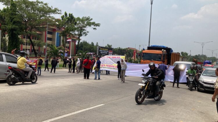 BENTANGKAN SPANDUK: Puluhan peserta PPPK Kabupaten Langkat membentangkan spanduk menutup jalan di depan Mapolda Sumut saat gelar aksi demo, Rabu (13/3/2024). (Foto Dok/T77)