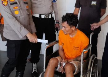 NB: Reza Adrian Siregar - PEMBUNUH DITEMBAK: Kapolsek Medan Tembung Kompol Jhonson Sitompul menginterogasi pelaku pembunuhan pedagang mie aceh berinisial RAS yang duduk di kursi roda usai kedua kakinya ditembak polisi, di Mapolsek, Jumat (26/7/2024).(Foto Dok/ Polrestabes)