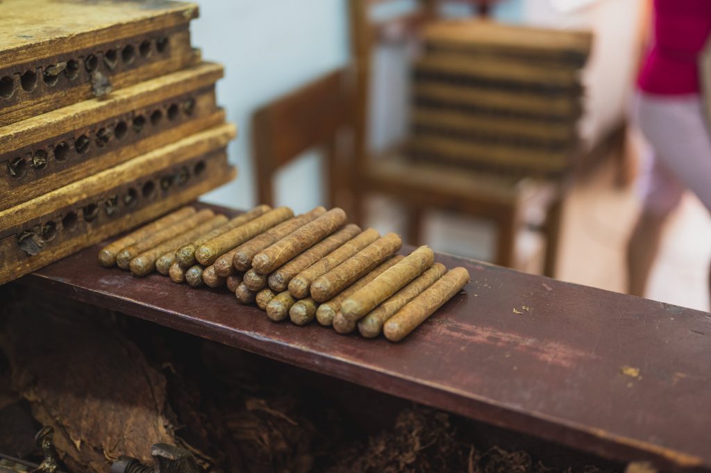https://www.pexels.com/id-id/foto/produksi-cerutu-mentah-di-atas-meja-kayu-di-kain-3975055/
